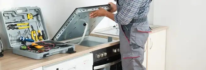 Cooktop repair technician lifting a built-in stovetop for service in Chula Vista, CA