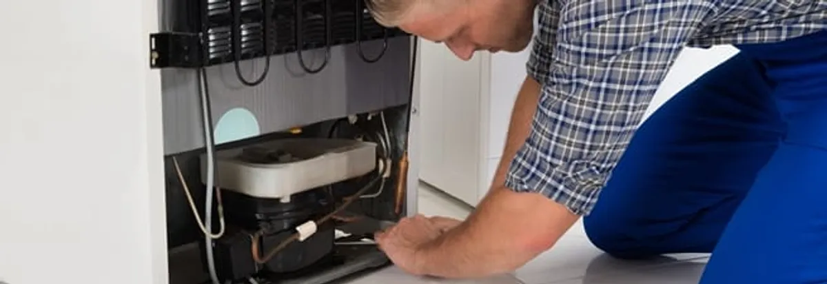 Refrigerator repair technician servicing the compressor and condenser area in Chula Vista, CA