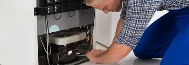 Refrigerator repair technician servicing the compressor and condenser area in Chula Vista, CA