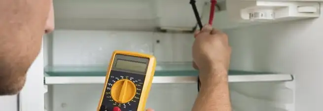 Refrigerator repair technician testing electrical components with a multimeter in Chula Vista, CA