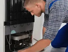 Refrigerator repair technician servicing the compressor and condenser area in Chula Vista, CA